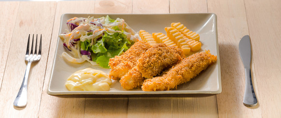 Deep fried fish steak served with french fries and fresh vegetables on white plate.