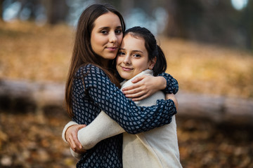 Fototapeta premium Portrait of two beautiful tennage sisters standing and posing in autumn park or forest. Natural light.