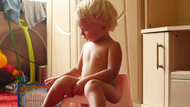 funny cute 18 monts old baby on chamberpot playing with book indoors
