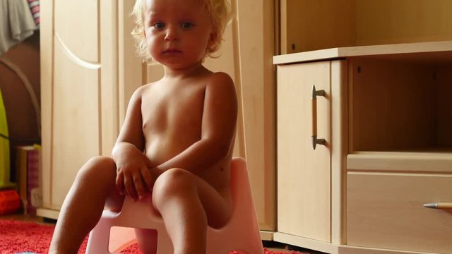 cute blond 1,5 years old baby boy on chamberpot indoors approaching camera