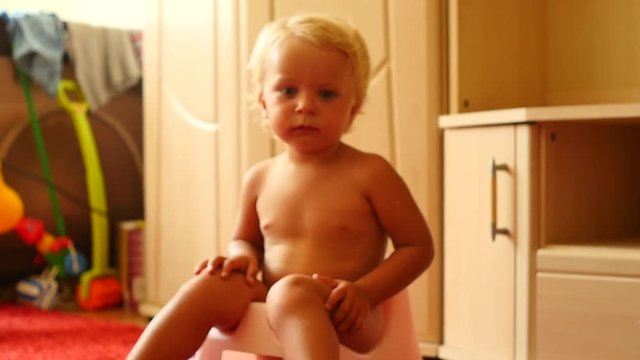 cute blond 1,5 years old baby boy on chamberpot indoors approaching camera