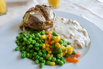 A meal of baked potato, chicken in white sauce and mixed vegetables on a white plate.