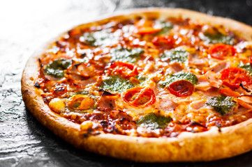 Pizza with Mozzarella cheese, Ham, Tomatoes, pepper, Spices and Fresh Basil pesto sauce. Italian pizza.on black background.