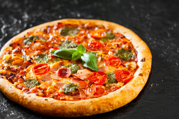 Pizza with Mozzarella cheese, Ham, Tomatoes, pepper, Spices and Fresh Basil pesto sauce. Italian pizza.on black background.