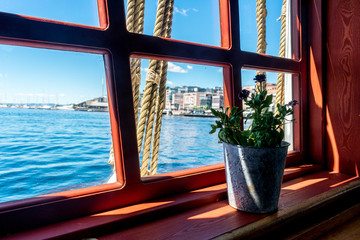 The view out the window of a boat looking out onto the bright blue ocean, with a flower pot on the window sill