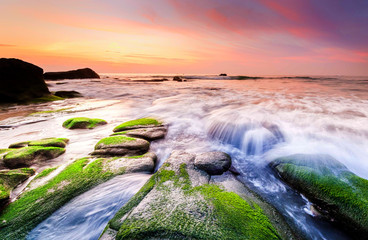 colorful sunset seascape with natural coastal rocks on the ground. soft focus due to slow shutter and water movement.