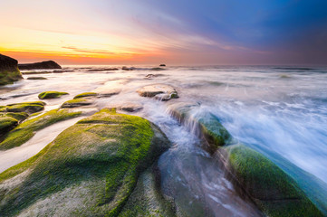 colorful sunset seascape with natural coastal rocks on the ground. soft focus due to slow shutter and water movement.