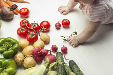 Little baby looks at fresh organic vegetables on a light wooden