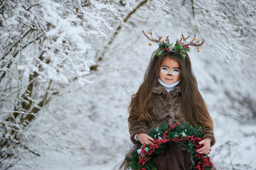 Fairy tale girl. Portrait a little girl in a deer dress with a painted face in the winter forest....