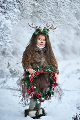 Fairy tale girl. Portrait a little girl in a deer dress with a painted face in the winter forest....