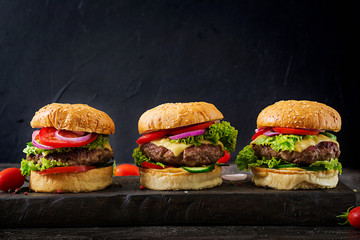 Three hamburger with beef meat burger and fresh vegetables on dark background. Tasty food.