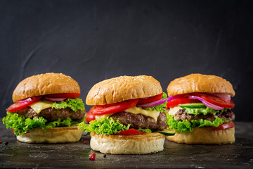 Three hamburger with beef meat burger and fresh vegetables on dark background. Tasty food.