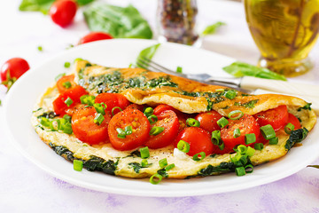 Omelette with tomatoes, spinach and green onion on white plate.  Frittata - italian omelet.