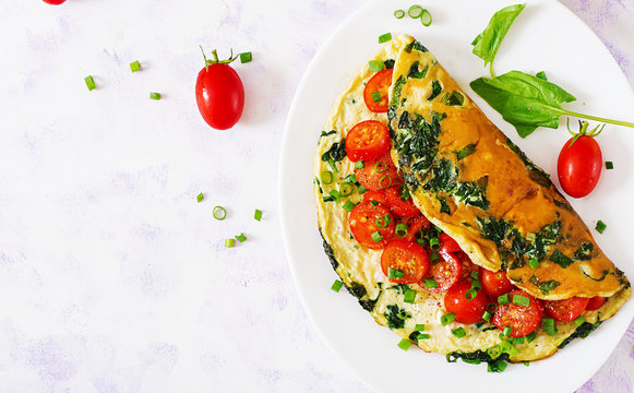 Omelette with tomatoes, spinach and green onion on white plate.  Frittata - italian omelet. Top view. Flat lay.