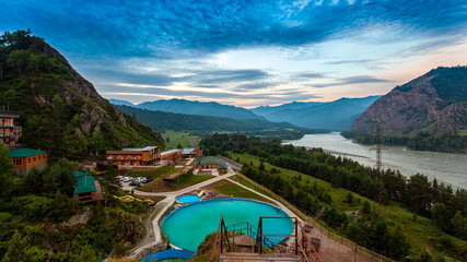Mountain panorama: a small village, a recreation center with a pool and small wooden houses in the mountains of Altai, near a mountain river and road
