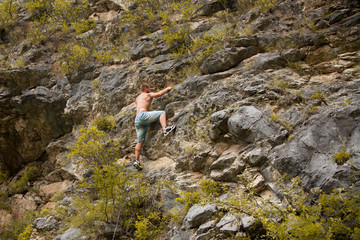 Rock climber. Strong young man climbing on a limestone wall with mountains and trees on the background. Conceptual scene of freedom and a strong, purposeful man