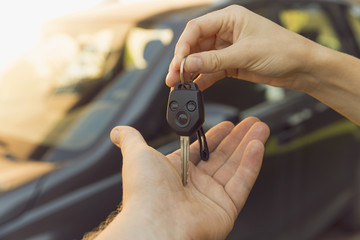 Woman dealer hand giving car keys to man, car on the background