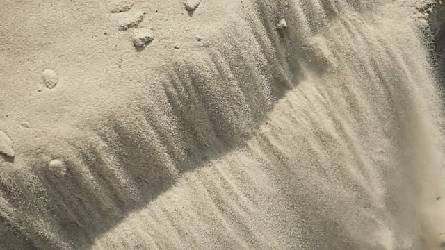 White fine sand avalanche slopes down the hill under sun light on sea, ocean, river coast or in desert. Abstract summer surface background. Closeup view. Slow motion