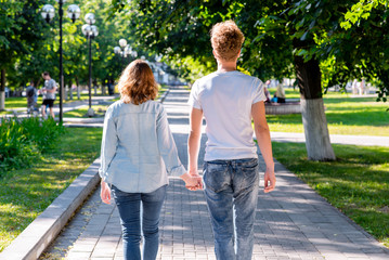 Obraz premium A guy with a girl in the summer in park holding hands walking in the park. Camping. The concept of love and happiness. The beginning of the relationship of the newlyweds. Back view.