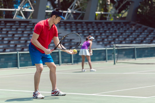 Side View Of An Asian Tennis Player Ready To Serve At The Beginning Of A Doubles Mixed Match On A Professional Tennis Court