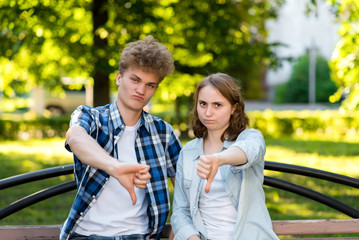 Obraz premium Young guy students with a girl. In the summer in park in nature. He gestures his finger down. Disco. The concept of distrust. Emotion does not work out well. Bad result.
