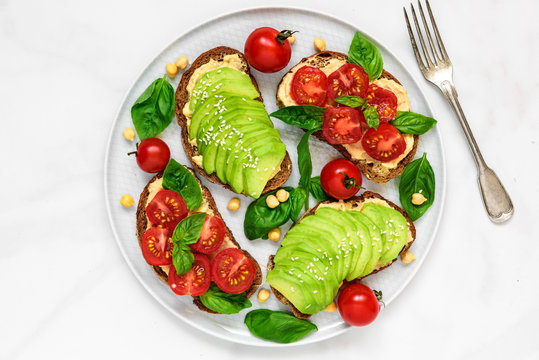 healthy avocado and tomatoes sandwiches with hummus, sesame and basil in a plate with fork