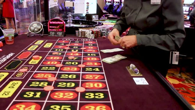 Dealer counting twenty dollar bills as she cashes in chips at the roulette table.