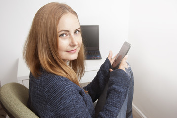 Young woman portret, working on laptop computer, freelancer. Smiling at camera. Wears blue sweater. Copy space.