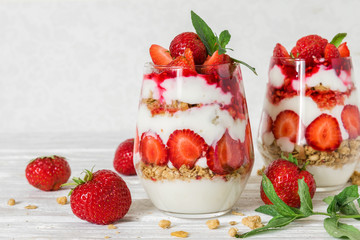 strawberry yogurt parfait with granola, mint and fresh berries in glasses on white wooden table....