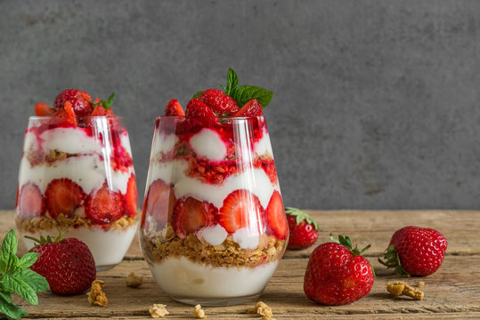 strawberry yogurt parfait with granola, mint and fresh berries in glasses on rustic wooden table. healthy breakfast