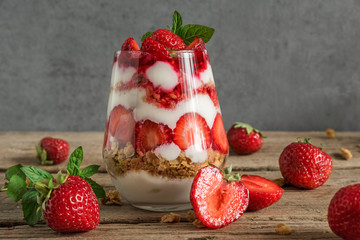 strawberry yogurt parfait with granola, mint and fresh berries in a glass on rustic wooden table....
