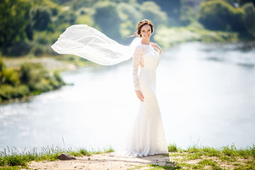 young beautiful bride girl with wedding bouquet of roses stands near the river. the wind blows the...