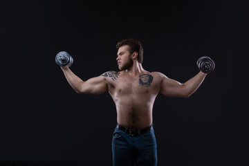 Fototapeta na wymiar Muscular bodybuilder guy doing exercises with dumbbells over black background