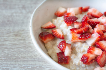 Rolled  organic porridge with strawberries in marble bowl  on wood table side view healthy breackfast