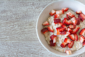 Top view of rolled  organic porridge with strawberries in marble bowl on wooden table  healthy breackfast