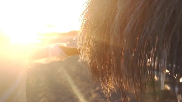 woman caucasian hand touching umbrella sun at the beach during a beautiful golden sunset. vacation and travel in tropical island concept. resort and happiness leisure activity for traveler holiday peo