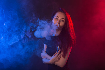 Portrait of girl in colored neon smoke with vape or electronic cigarette.