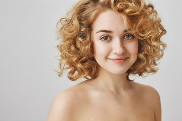 Naklejka premium Body positive and beauty concept. Attractive european female student with blonde curly hair standing naked over gray background, smiling sensually at camera, expressing positive attitude.