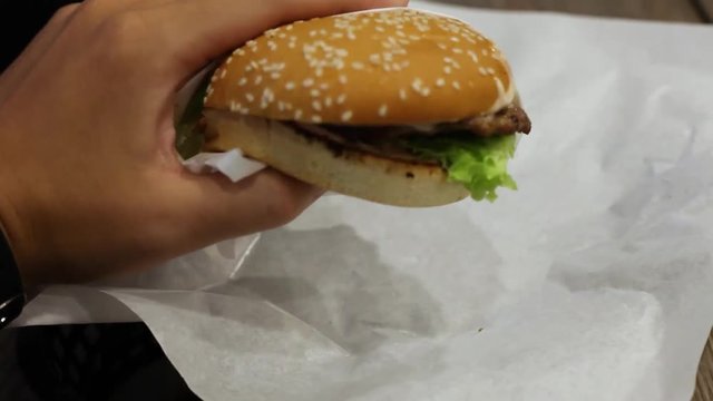 Holding burger with left hand and hand it to the camera. First person of a man eating a buger