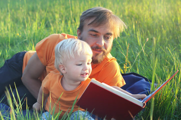 Father and his cute toddler son read book together outdoor. Authentic lifestyle image. Parenting or childhood concept