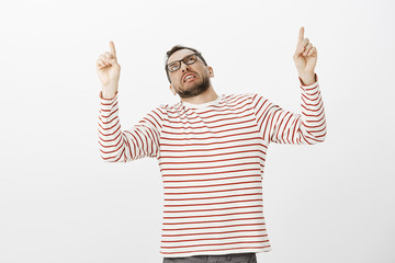 Indoor shot of displeased disgusted adult guy in fancy striped pullover, pointing and looking up...