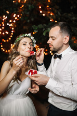 Happy bride and groom cut the wedding cake in the front garland light decoration. Wedding evening outdoor. Sweet happy life concept