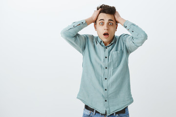 Portrait of anxious troubled handsome man in casual outfit, dropping jaw from shock and touching hair nervous, feeling clueless what to do, worrying about losing job over gray background