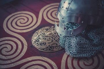viking helmet with chain mail on a red shield with golden shapes of sun, weapons for war
