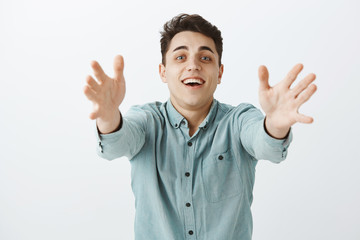 Waist-up shot of happy grinning young man in casual shirt, pulling hands towards camera and smiling tenderly, feeling temptation and passion, wanting cuddle friend over gray background