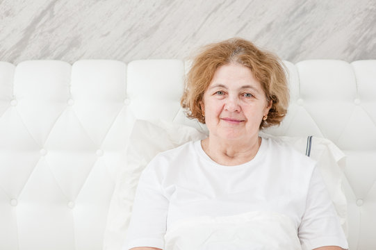 Happy senior woman sitting on the bed. Space for text