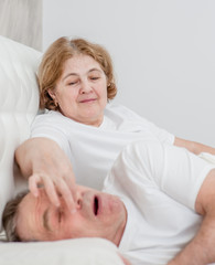senior woman covers husband`s nose, can`t sleep because of his snoring