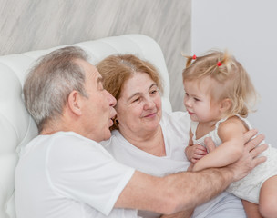 Grandparents is having fun with his granddaughter on the bed