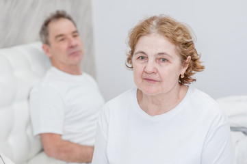 Sad senior couple sitting on bed at home