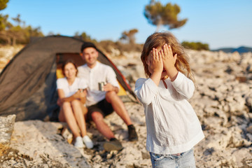 Pretty girl standing on rocky beach and closing eyes covering face with hand.